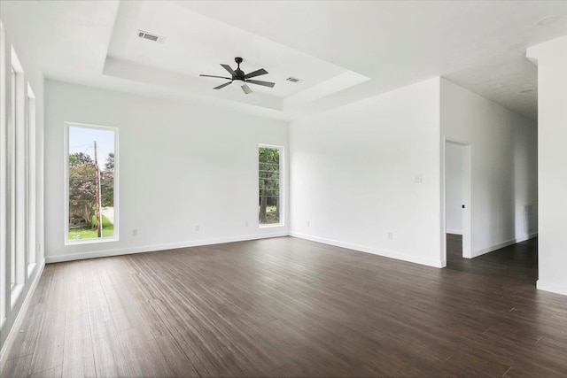 spare room with ceiling fan, dark hardwood / wood-style flooring, a raised ceiling, and a wealth of natural light