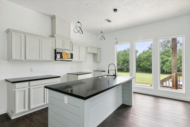 kitchen featuring dark hardwood / wood-style flooring, a kitchen island with sink, sink, and decorative light fixtures