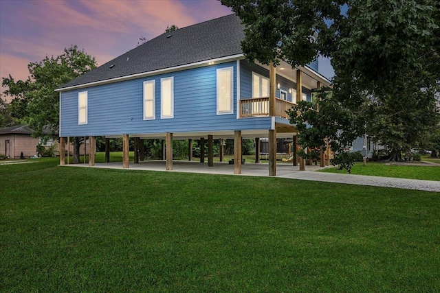 back house at dusk featuring a lawn and a balcony