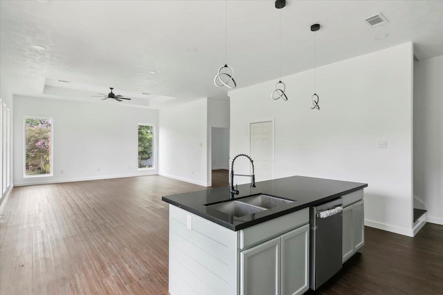 kitchen featuring sink, a raised ceiling, stainless steel dishwasher, pendant lighting, and a center island with sink