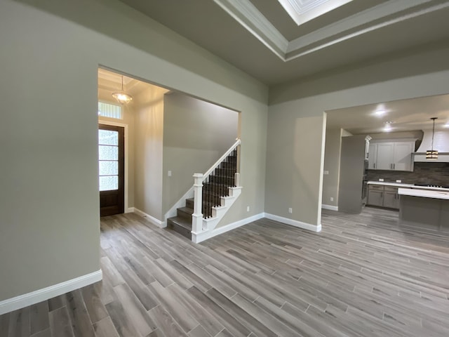 unfurnished living room featuring a raised ceiling, light wood-type flooring, a notable chandelier, and ornamental molding