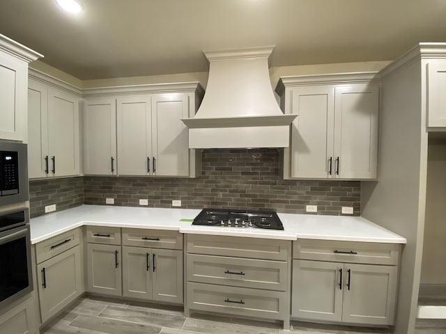 kitchen featuring backsplash, gray cabinetry, custom range hood, and stainless steel appliances