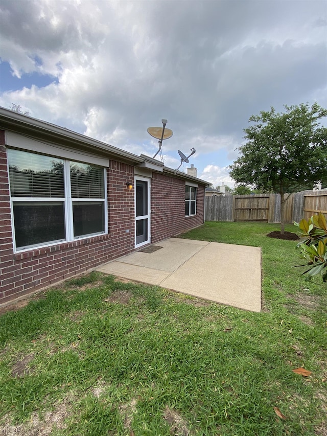 rear view of house with a patio, brick siding, a fenced backyard, and a lawn