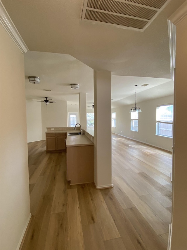 hall featuring a sink, baseboards, light wood finished floors, and visible vents