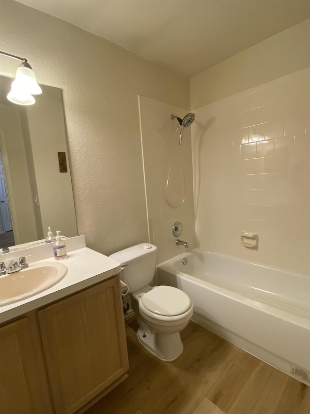 bathroom with vanity, a textured wall, wood finished floors, toilet, and bathtub / shower combination