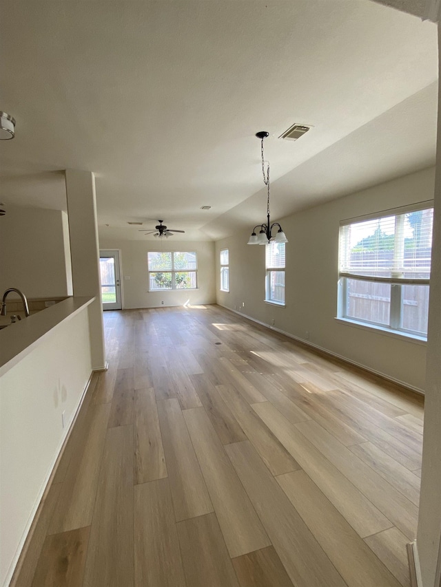 unfurnished dining area with visible vents, a sink, baseboards, ceiling fan with notable chandelier, and light wood-style flooring