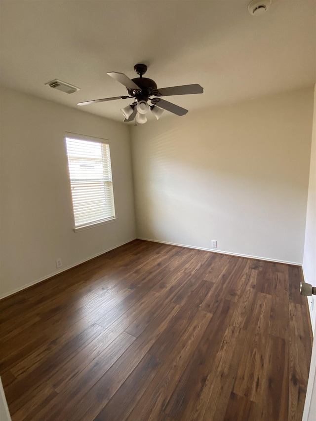 empty room featuring ceiling fan, visible vents, and dark wood finished floors