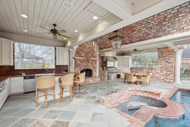 view of patio with area for grilling, grilling area, an outdoor brick fireplace, a bar, and ceiling fan