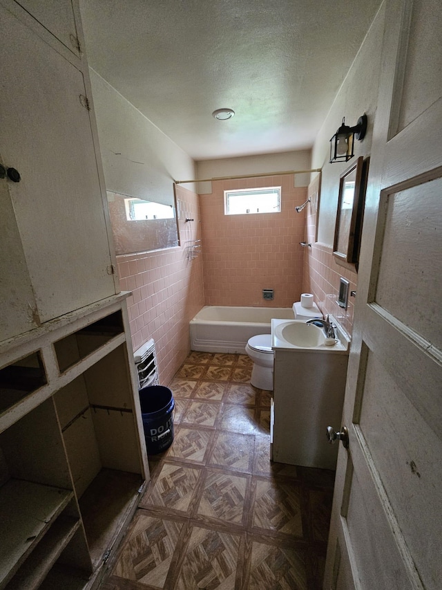 bathroom with tile walls, toilet, vanity, shower / tub combination, and a textured ceiling