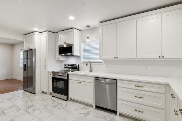 kitchen with decorative light fixtures, stainless steel appliances, white cabinetry, and sink