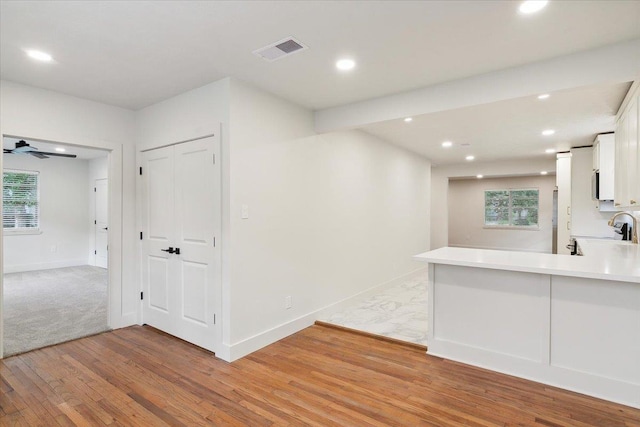 kitchen featuring kitchen peninsula, light wood-type flooring, white cabinets, and ceiling fan