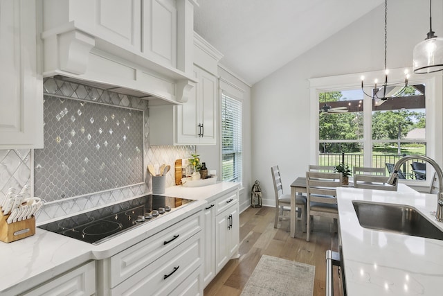 kitchen with lofted ceiling, plenty of natural light, white cabinets, black electric cooktop, and a sink