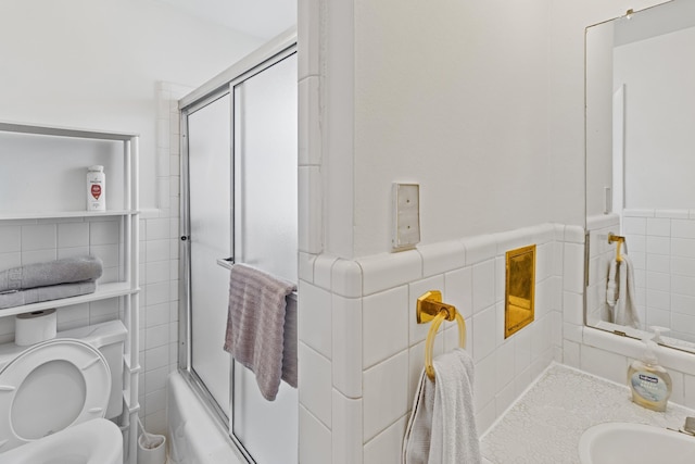 full bathroom featuring combined bath / shower with glass door, vanity, toilet, and tile walls