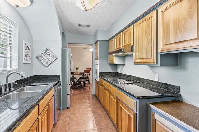 kitchen with sink, stainless steel appliances, dark stone countertops, a textured ceiling, and light tile patterned flooring