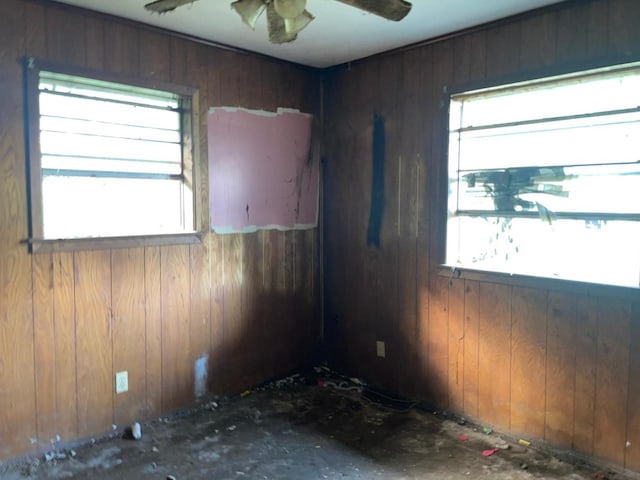 empty room featuring plenty of natural light, wood walls, and ceiling fan