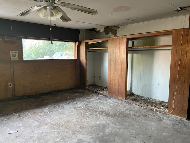 unfurnished bedroom with concrete flooring, ceiling fan, multiple closets, and wood walls