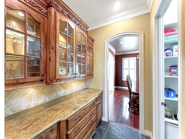 bar featuring light stone countertops, tasteful backsplash, dark wood-type flooring, and ornamental molding