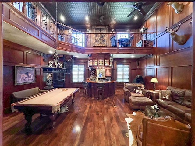 rec room with ceiling fan, wooden walls, hardwood / wood-style flooring, a high ceiling, and pool table