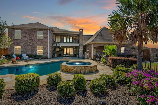 pool at dusk featuring a patio area and an in ground hot tub