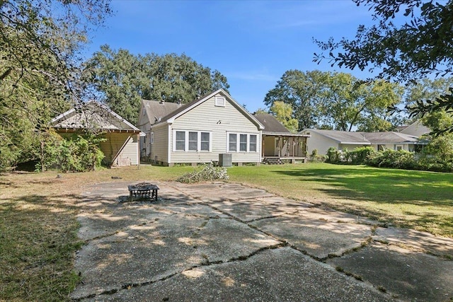 rear view of house with a sunroom, a yard, and a fire pit