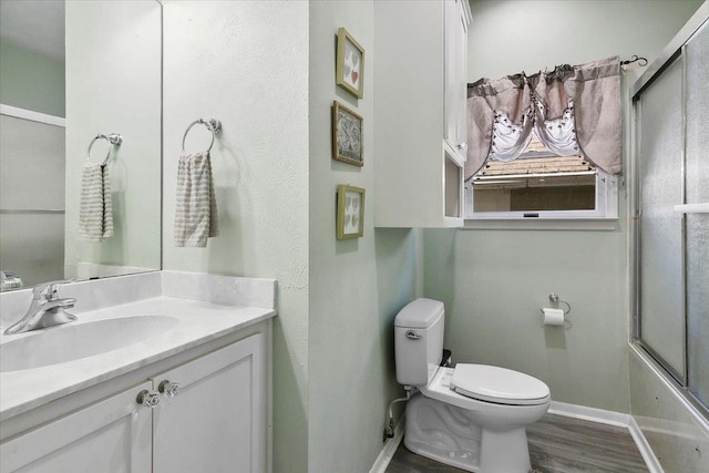 full bathroom featuring hardwood / wood-style flooring, vanity, toilet, and combined bath / shower with glass door