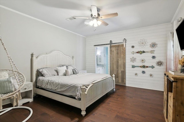 bedroom with ensuite bathroom, wooden walls, ceiling fan, a barn door, and dark hardwood / wood-style floors