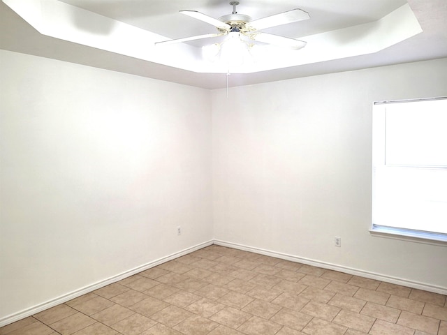 empty room with ceiling fan and a raised ceiling