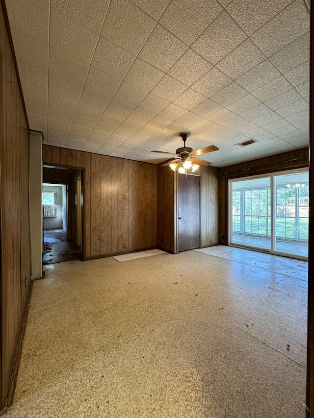 empty room with ceiling fan and wood walls