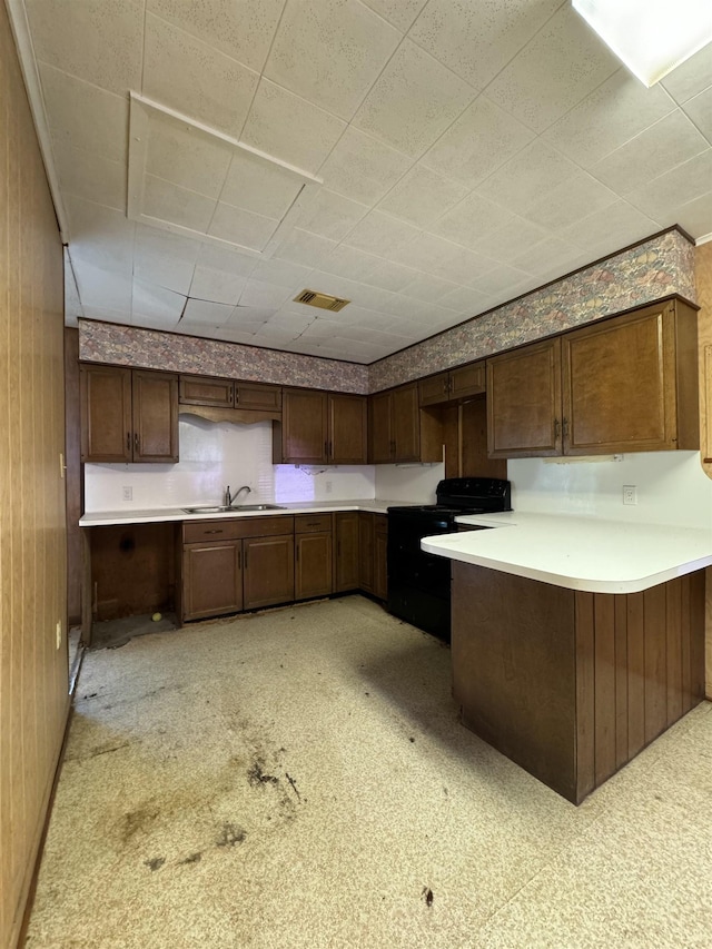 kitchen featuring sink, black electric range oven, kitchen peninsula, wooden walls, and dark brown cabinets