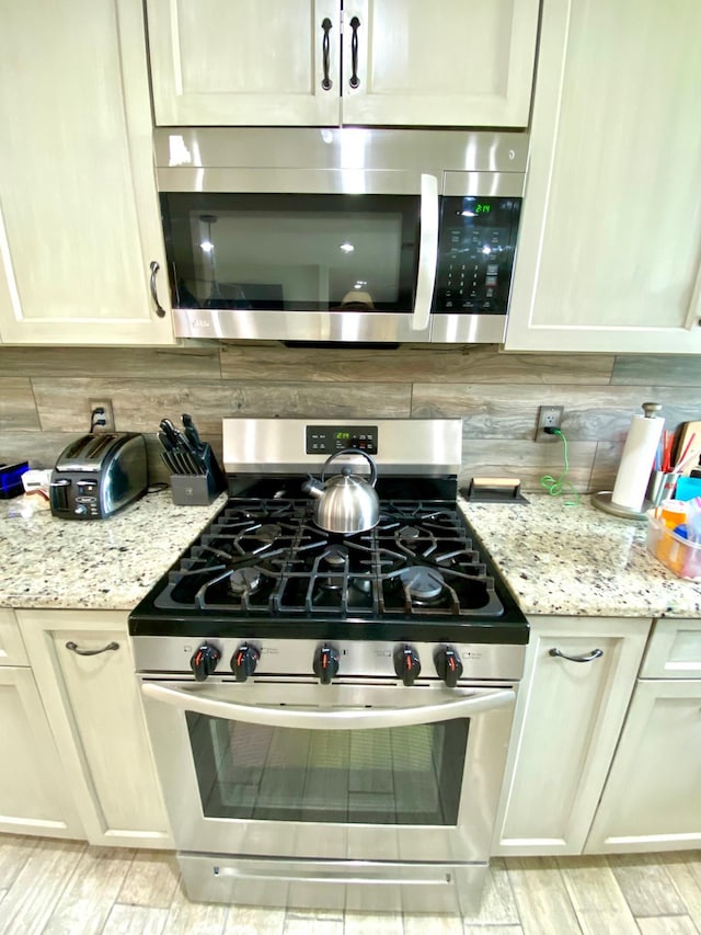 kitchen featuring tasteful backsplash, light stone countertops, and appliances with stainless steel finishes