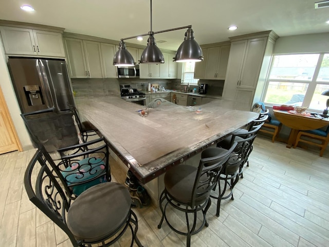 kitchen with a breakfast bar, appliances with stainless steel finishes, light hardwood / wood-style flooring, and pendant lighting