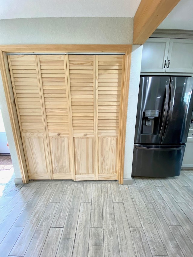 kitchen featuring stainless steel refrigerator with ice dispenser, light wood-type flooring, and beam ceiling