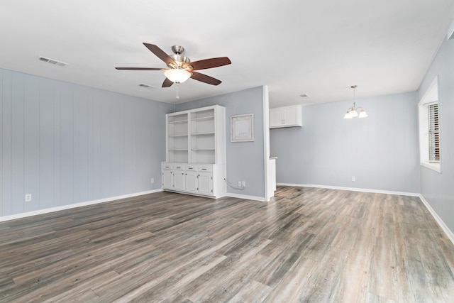 unfurnished living room with ceiling fan with notable chandelier, visible vents, baseboards, and wood finished floors