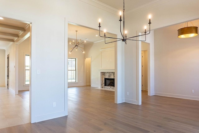 unfurnished living room featuring wood-type flooring, a premium fireplace, ornamental molding, and a chandelier