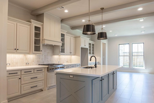 kitchen featuring stainless steel gas stovetop, a center island with sink, sink, hanging light fixtures, and decorative backsplash