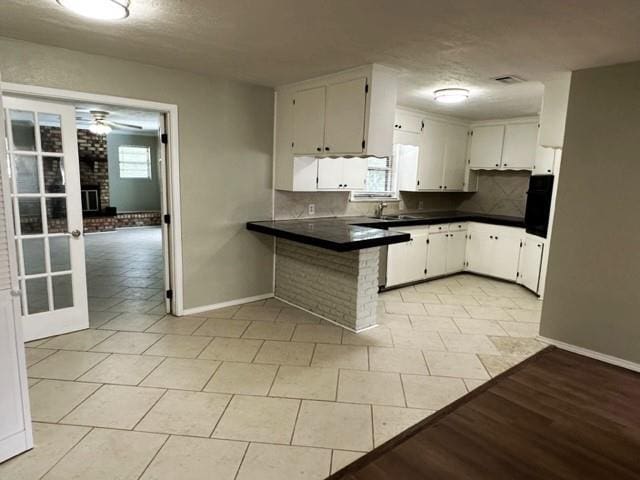 kitchen featuring sink, light tile patterned floors, kitchen peninsula, a fireplace, and white cabinets