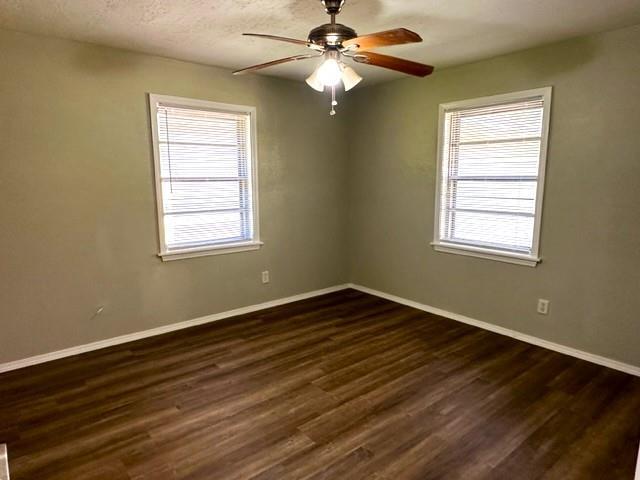 spare room featuring a textured ceiling, plenty of natural light, dark wood-type flooring, and ceiling fan