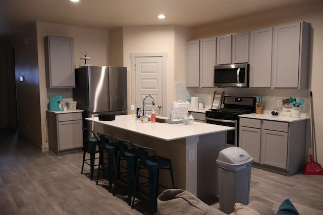 kitchen featuring stainless steel appliances, a kitchen island with sink, light hardwood / wood-style flooring, and gray cabinetry