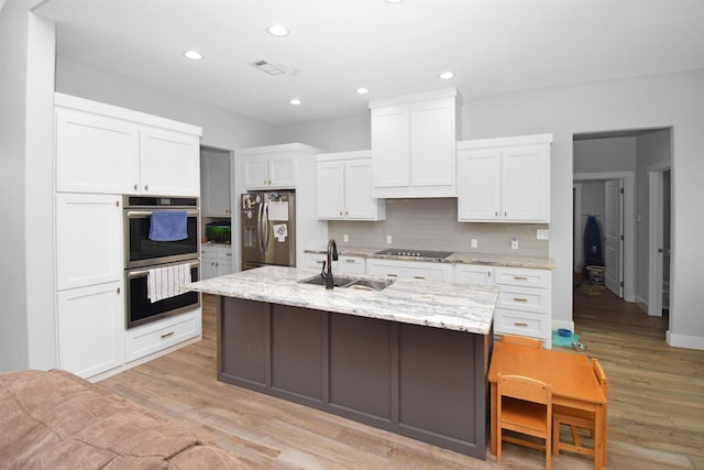 kitchen with sink, stainless steel appliances, light stone counters, a center island with sink, and white cabinets