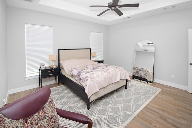 bedroom with ceiling fan, a raised ceiling, and wood-type flooring