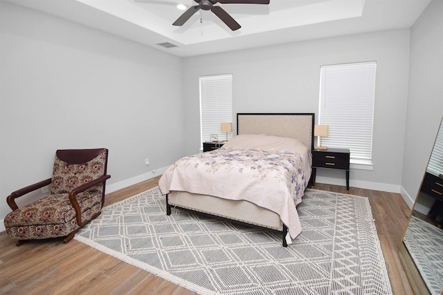 bedroom featuring ceiling fan, wood-type flooring, and a tray ceiling