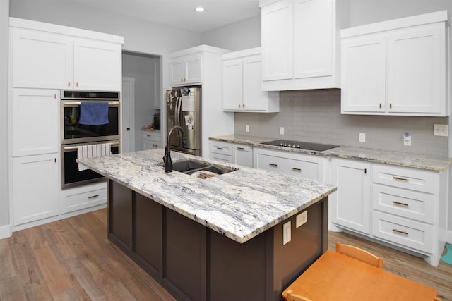 kitchen with white cabinets, appliances with stainless steel finishes, an island with sink, and sink