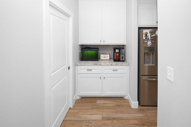 kitchen featuring stainless steel refrigerator with ice dispenser, tasteful backsplash, light stone counters, white cabinets, and light hardwood / wood-style floors