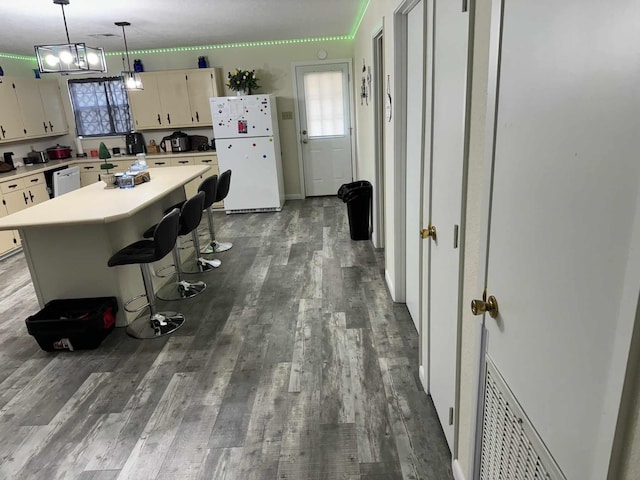 kitchen featuring a breakfast bar, white appliances, pendant lighting, wood-type flooring, and a center island