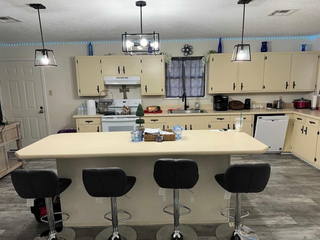 kitchen featuring sink, cream cabinets, a textured ceiling, white appliances, and a kitchen island