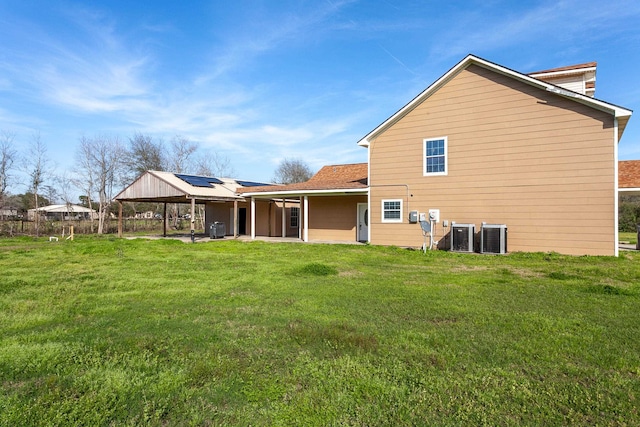 rear view of property with solar panels, central AC unit, and a lawn