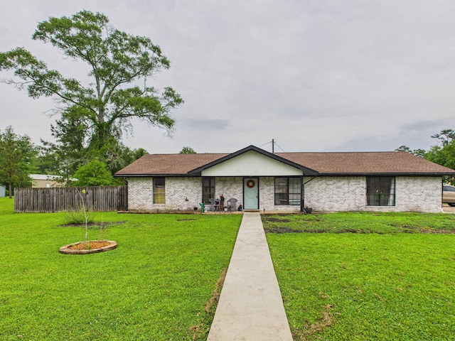 ranch-style home featuring fence, roof with shingles, a front yard, and brick siding