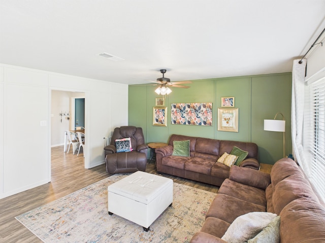 living area featuring a decorative wall, ceiling fan, wood finished floors, and baseboards