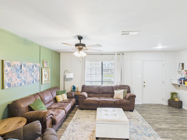 living room with a textured ceiling, wood finished floors, a ceiling fan, and visible vents