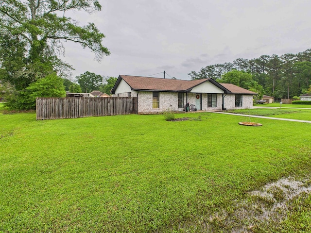 ranch-style home featuring fence, brick siding, a shingled roof, and a front lawn